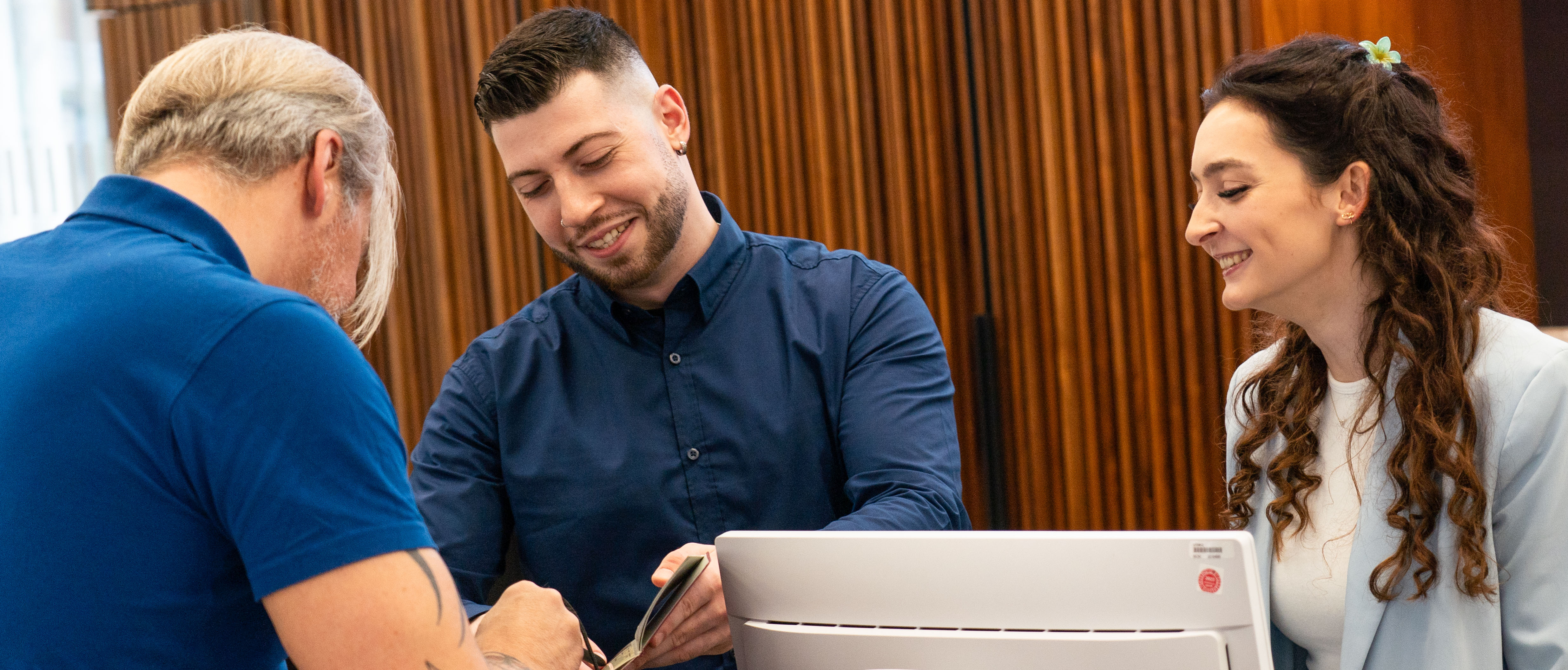 Zwei Personen stehen hinter einer Servicetheke und geben einem Mann vor der Theke Auskunft.