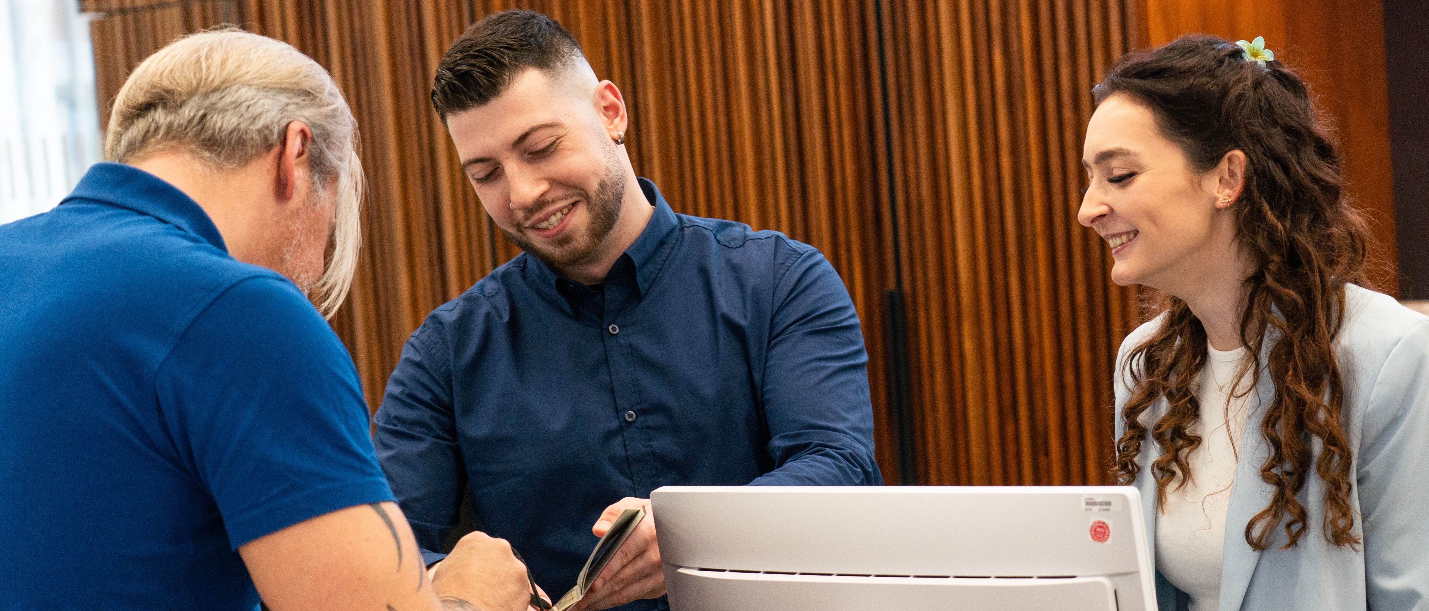 Zwei Personen stehen hinter einer Servicetheke und geben einem Mann vor der Theke Auskunft.