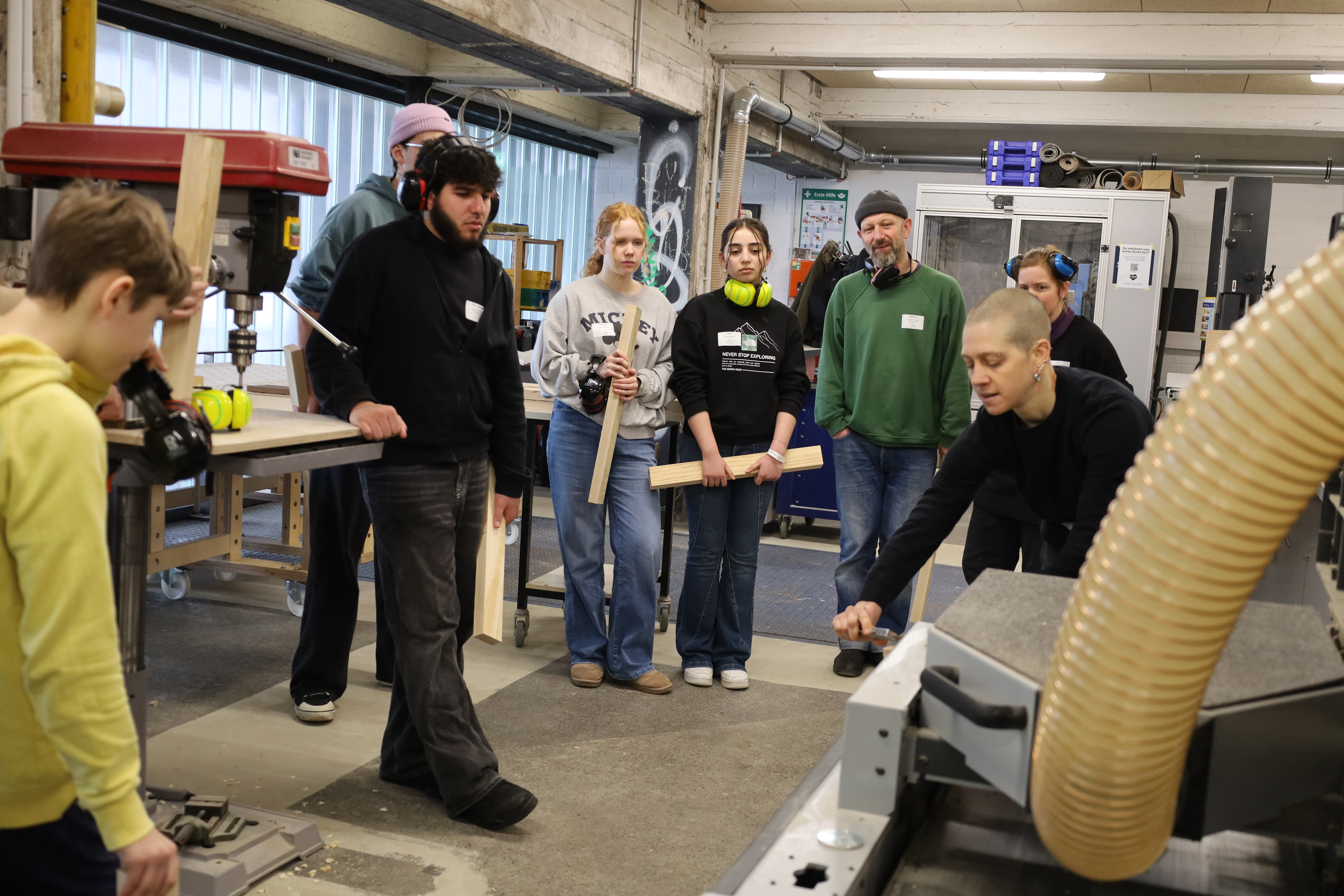 Eine Mitarbeiterin der HansaWerstatt in der B-Side zeigt Teilnehmenden am Workshop wie eine Holzlatte gehobelt wird.