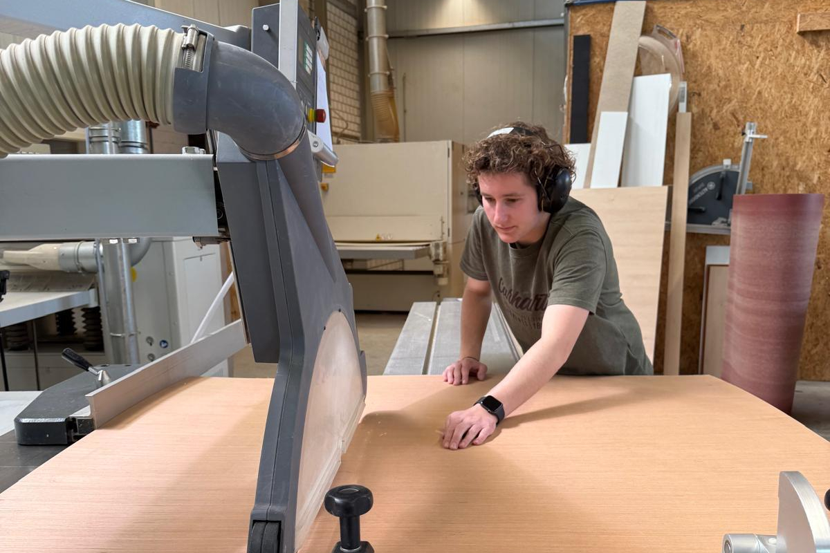 Tischlerin Anna Ahlers steht an einer großen Holzsäge und bearbeitet eine Holzplatte.