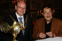 Rechts Oberbürgermeister Markus Lewe, links Günter Grass, der einen Stift zum Eintrag ins Goldene Buch in der Hand hält. Vor ihnen der geöffnete Goldene Hahn.