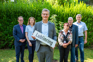 sechs Menschen stehen vor einem kleinen Baum. Der Mann in der Mitte hält ein Schild in der Hand, auf dem "Lublinring" steht. 