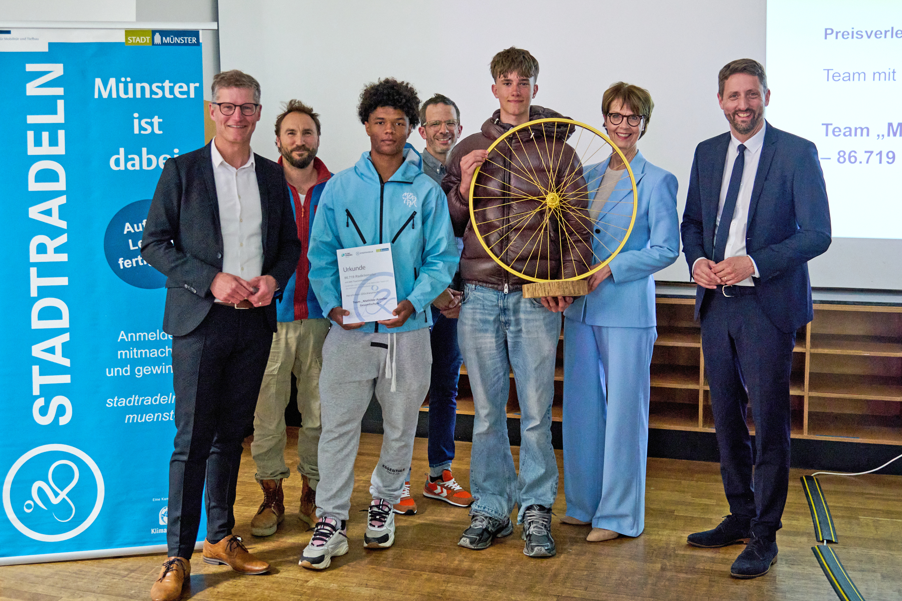 Eine Gruppe von Menschen lächelt in die Kamera, die mittleren zwei halten ein goldenes Rad