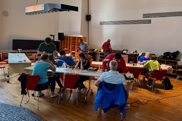 Personen sitzen zusammen um einen Tisch im Lesesaal der Bibliothek und basteln an Geräten im Repair-Café