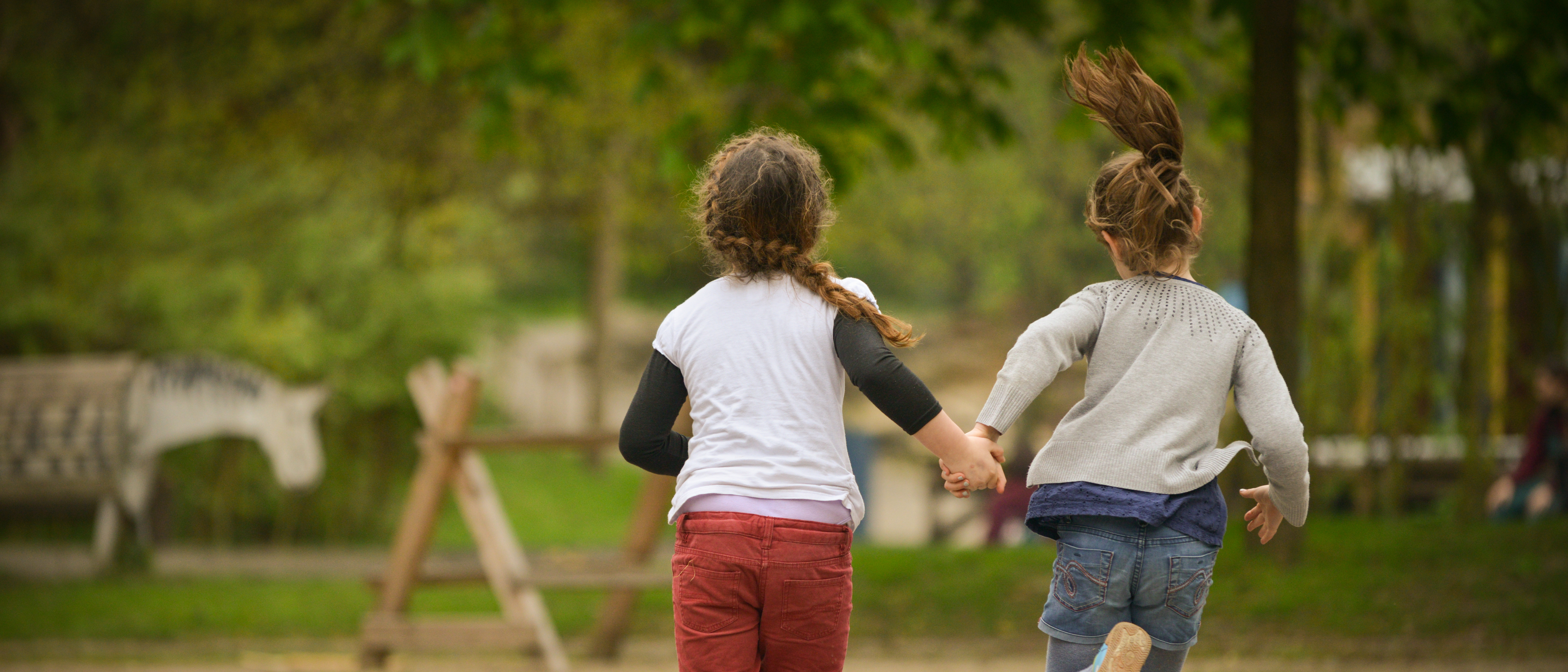 Zwei Mädchen laufen Hand in Hand über einen Spielplatz