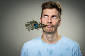 Portraitfoto von Simon Stäblein mit Pfauenfeder im Mund