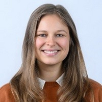 Junge Frau mit braunem Pullover und langen Haaren lächelt.