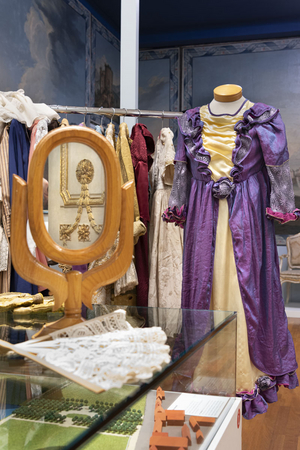 Eine Figurine trägt ein violettes Kleid im Ausstellungsraum zum Thema münsterisches Schloss. Im Vordergrund steht ein Spiegel. Viele Kostüme im Hintergrund. 