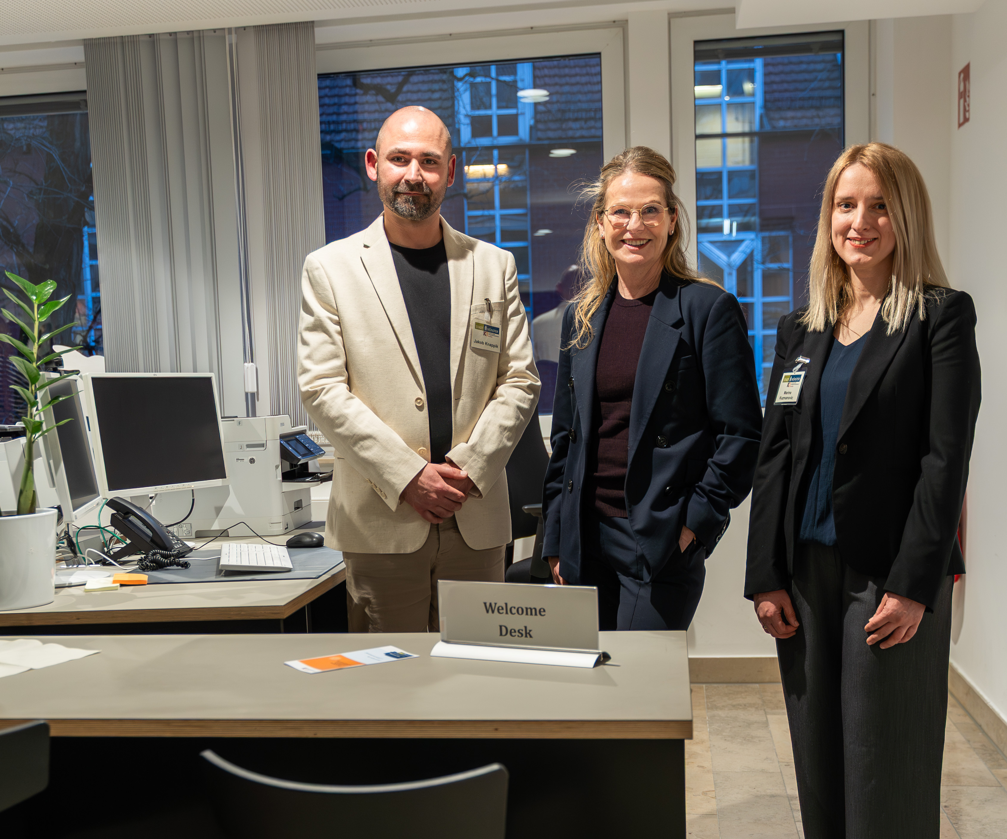 Drei Personen stehen im Büro hinter dem „Welcome Desk“