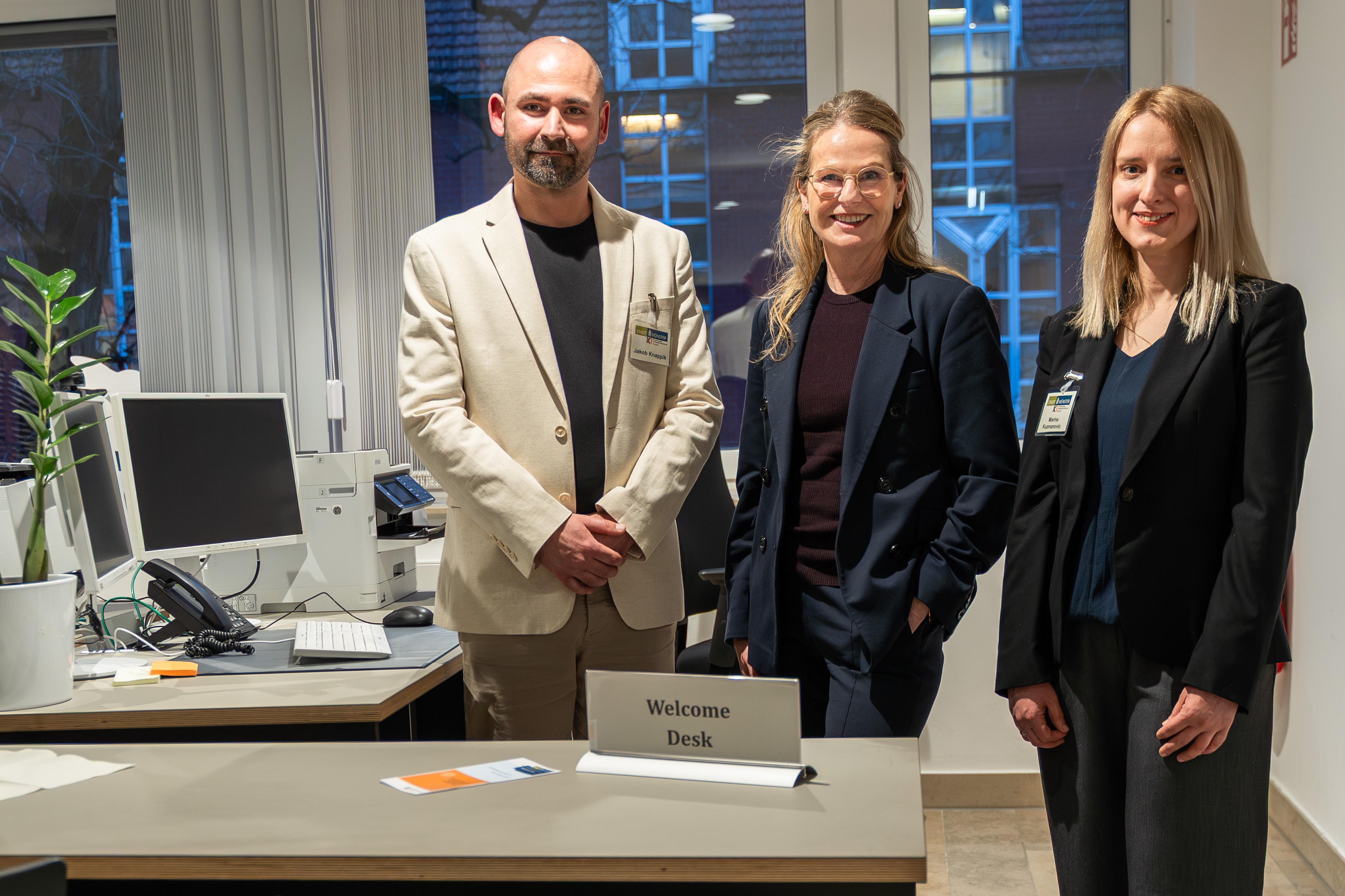 Drei Personen stehen im Büro hinter dem „Welcome Desk“