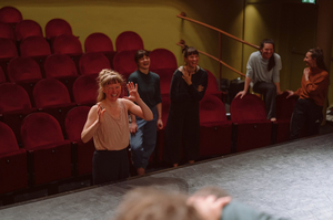 Die Tanz- und Theaterpädagogin Isabel Bernhard steht lachend mit offenen Armen zur Bühne blickend im Publikumsraum eines Theaters.