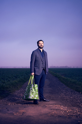 Portraitfoto Sulaiman Masomi mit grüner Tasche auf einem Feldweg vor Sonnenaufgang