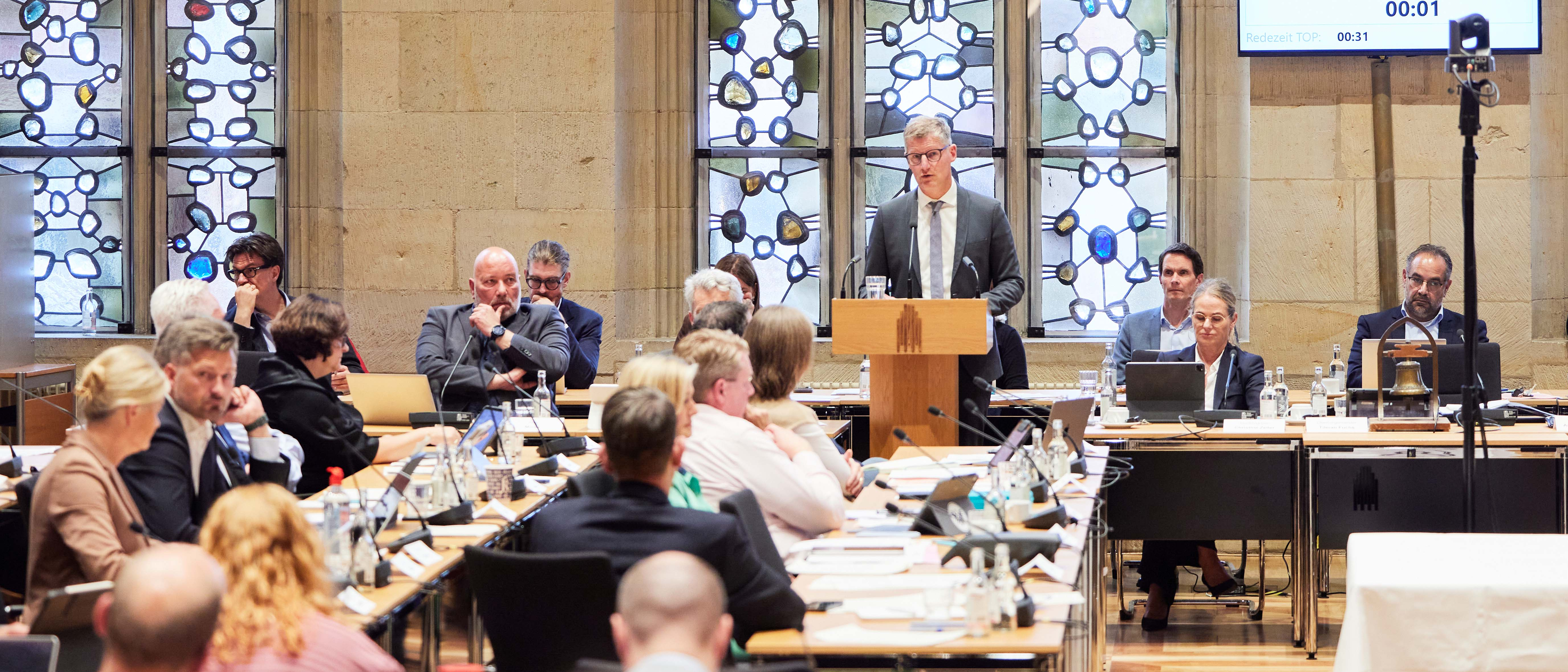 Blick in die Ratssitzung, Oberbürgermeister Tilman Fuchs steht am Rednerpult. Andere Ratsmitglieder sitzen an ihren Plätzen.