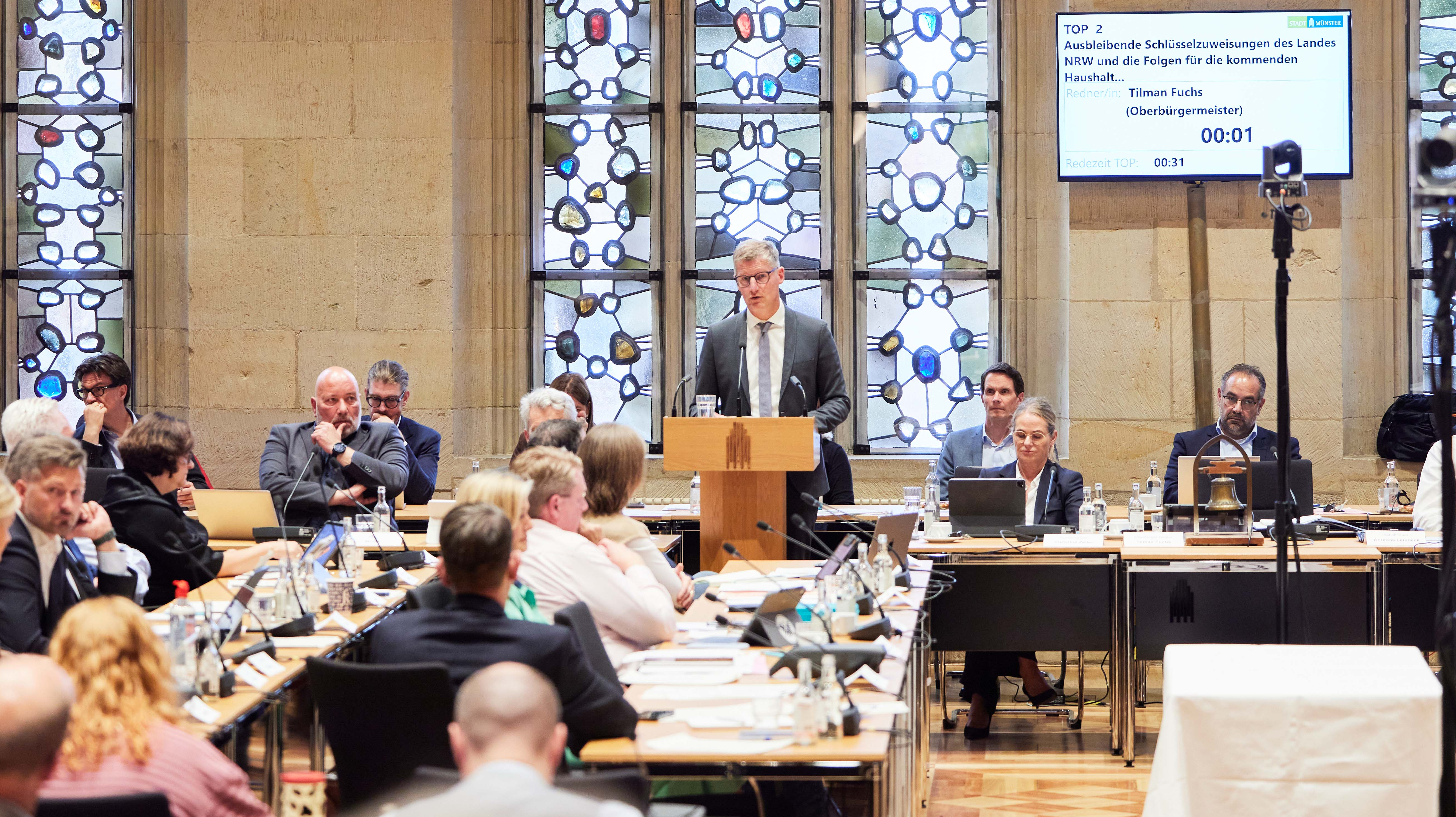 Blick in die Ratssitzung, Oberbürgermeister Tilman Fuchs steht am Rednerpult. Andere Ratsmitglieder sitzen an ihren Plätzen.
