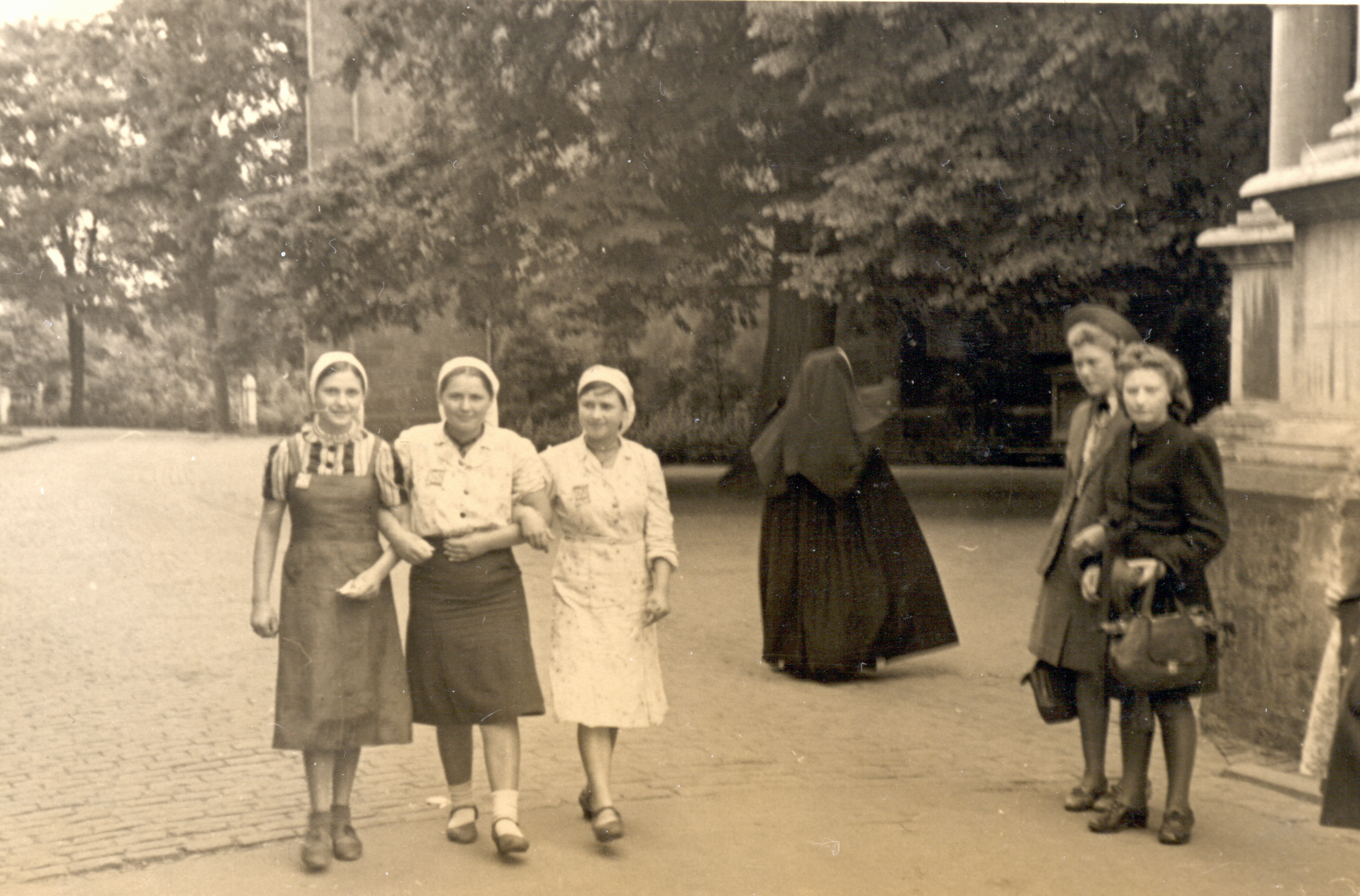 Sechs Personen in der Innenstadt: Im Zentrum stehen drei unter den Armen eingehakte junge Frauen mit „Ost“-Abzeichenvon.