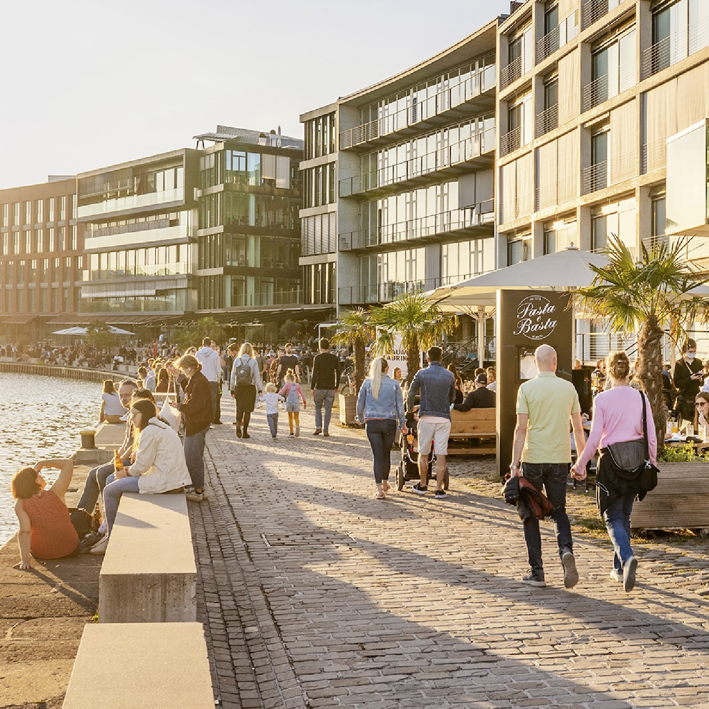 Personen flanieren am Hafen bei tief stehender Sonne