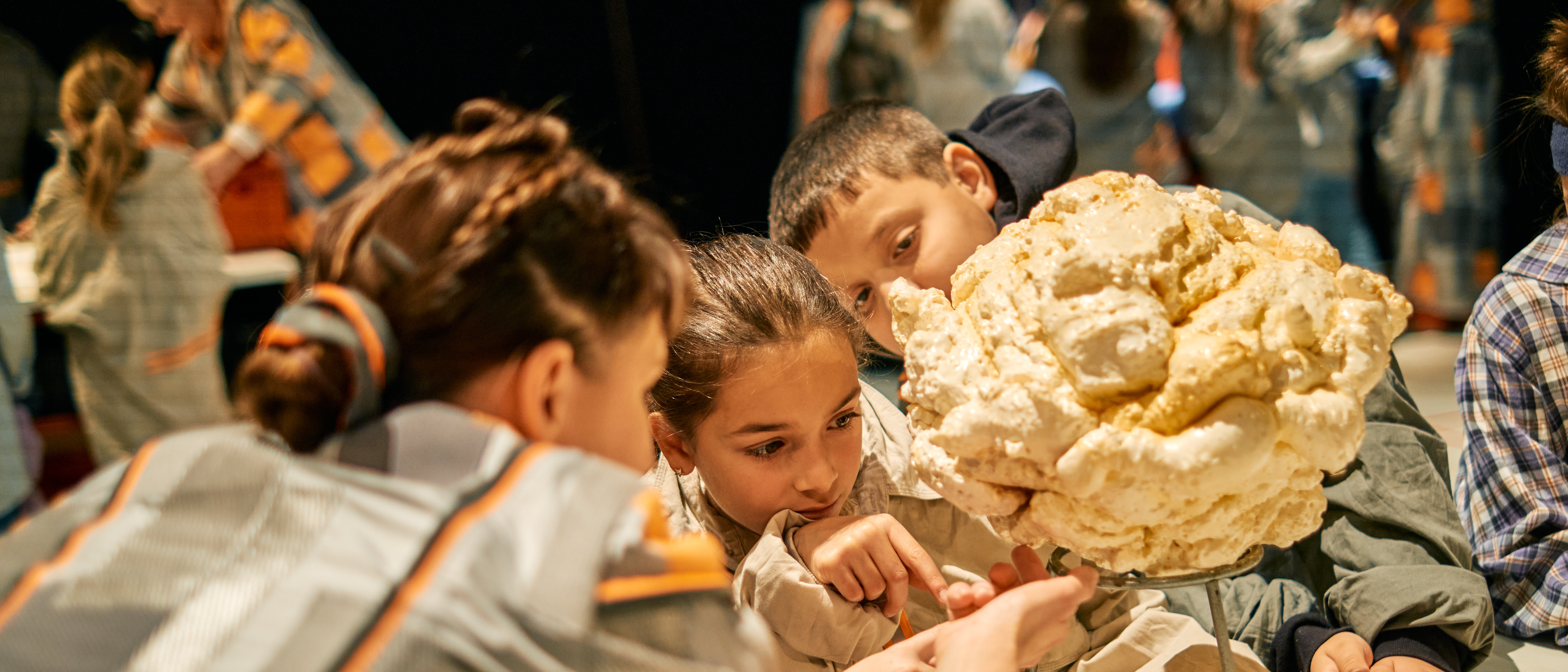 Eine Gruppe von Kindern schaut interessiert auf ein großes Model eines Popcorns.