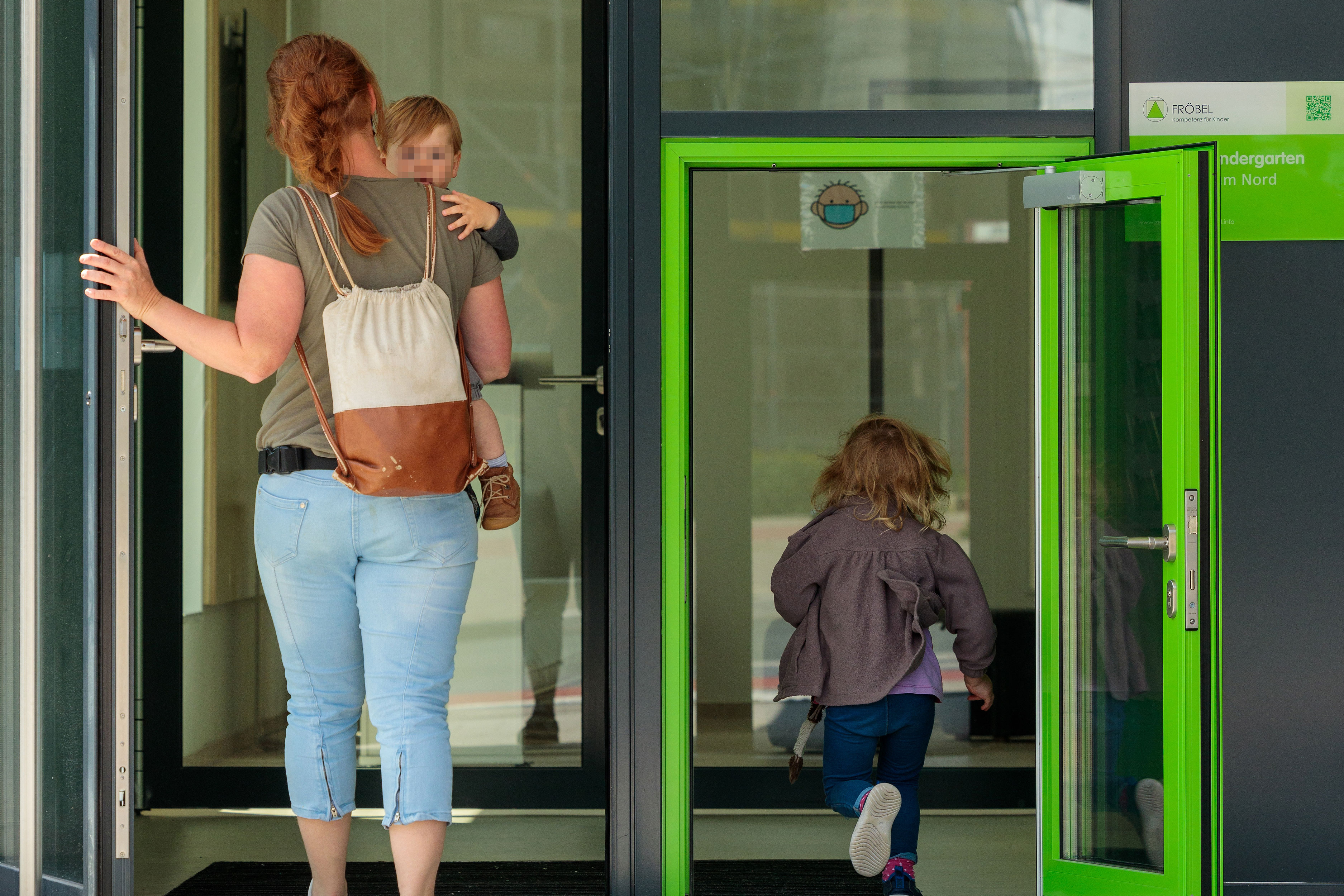 Eine Frau mit zwei Kindern betritt die Kita