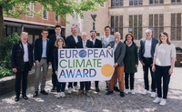 Eine Gruppe von Amtspersonen steht auf einem Platz und hält ein Transparent mit der Aufschrift "European Climate Award" hoch.