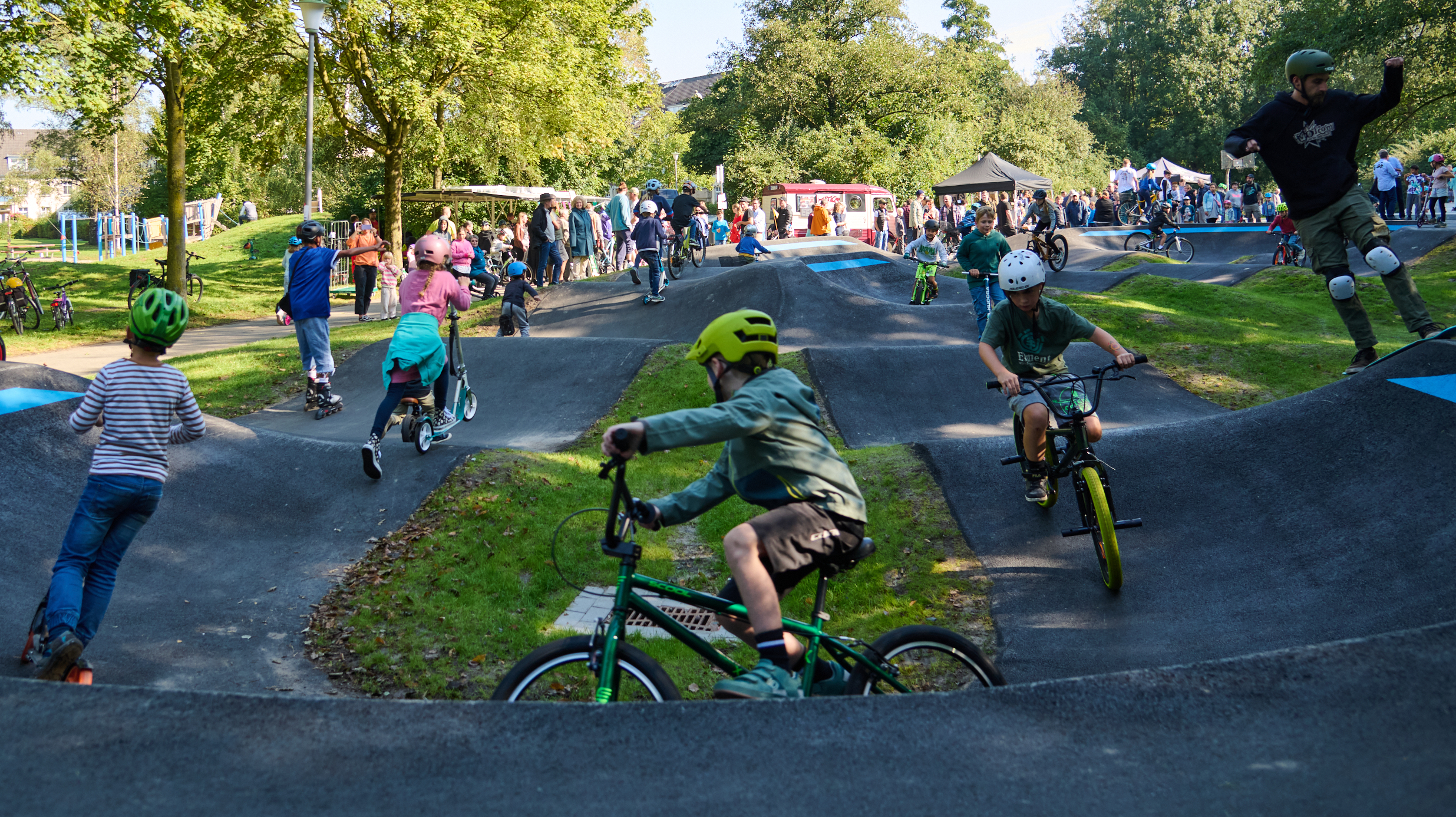 Kinder, die mit Fahrrad oder Roller über eine Pumptrachbahn fahren