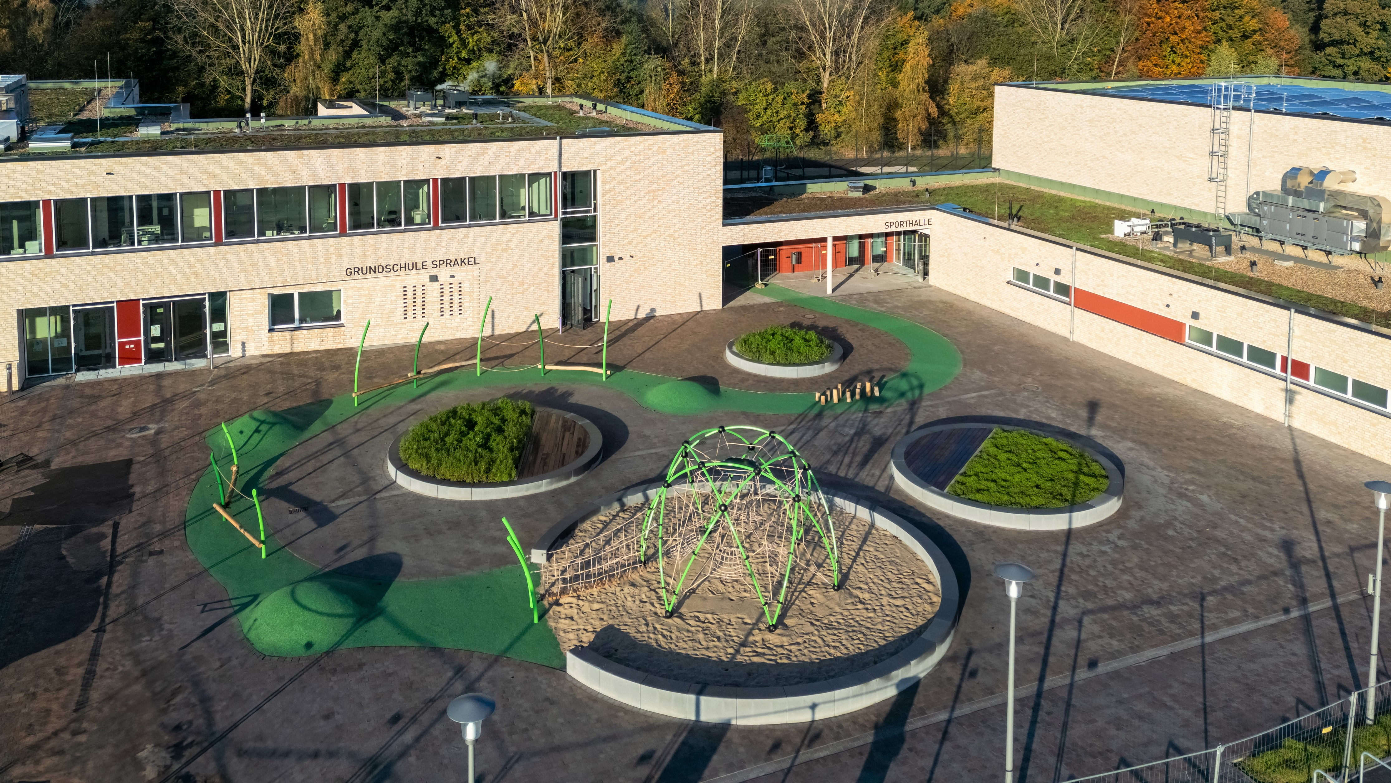 Ansicht der Grundschule von einem erhöhten Punkt. Im Mittelpunkt ist der von Schulgebäuden umgebene Schulhof mit runden Beeten.