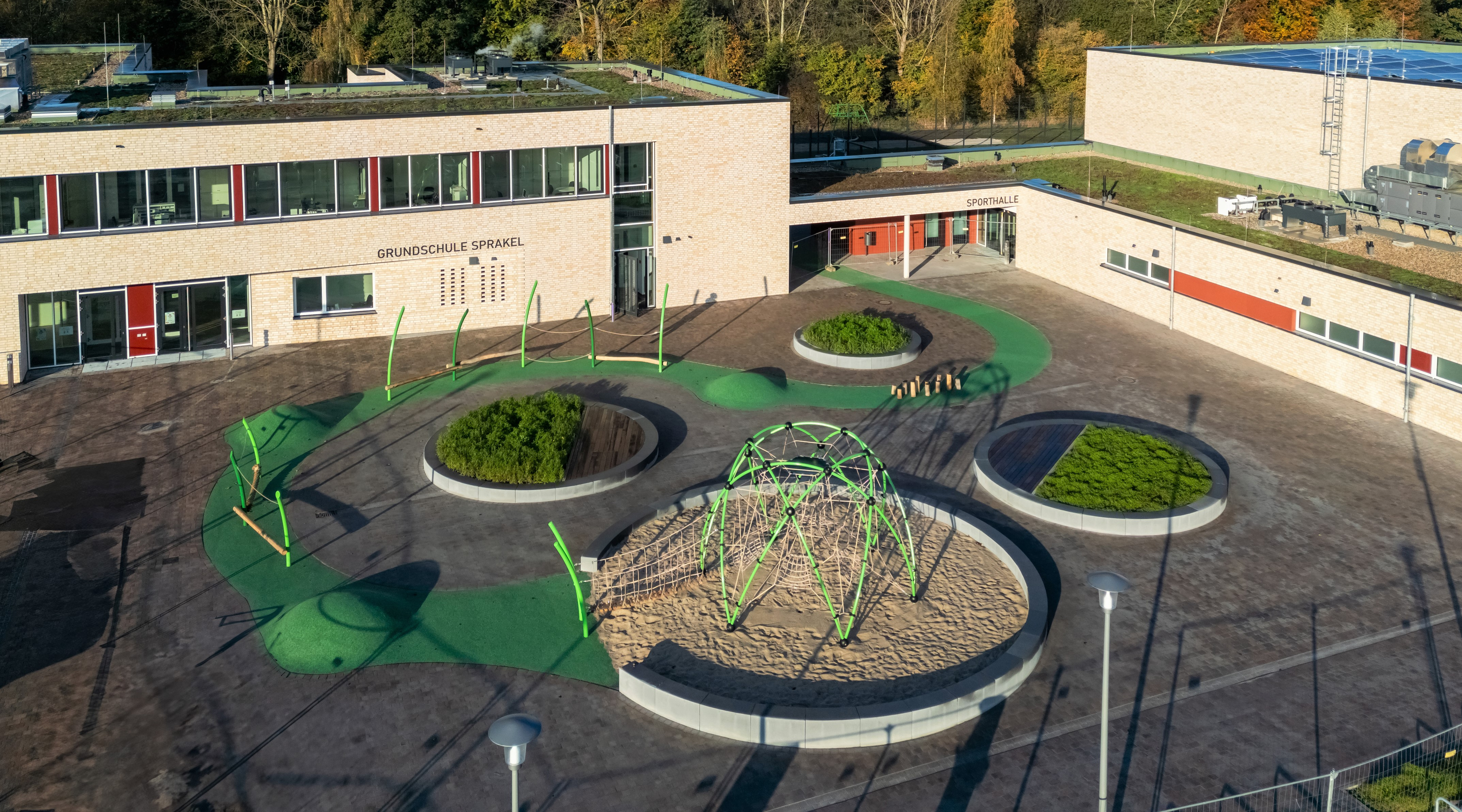 Ansicht der Grundschule von einem erhöhten Punkt. Im Mittelpunkt ist der von Schulgebäuden umgebene Schulhof mit runden Beeten.