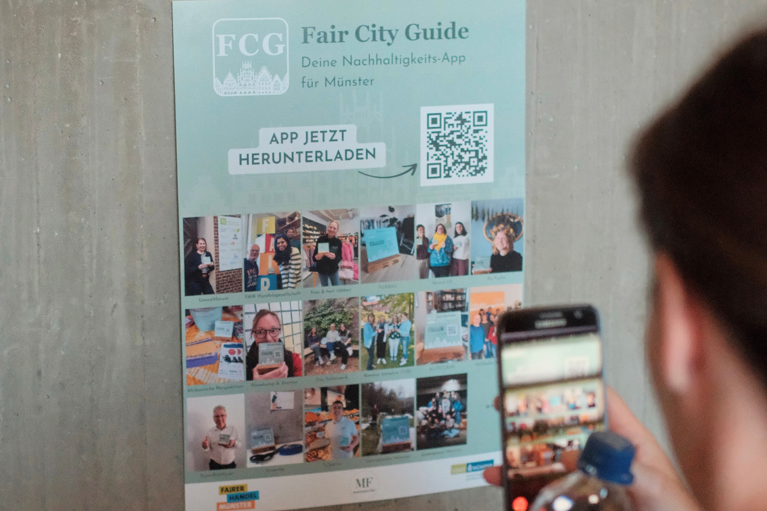Plakat für die Fair City Guide App mit QR-Code an einer Betonwand, eine Person fotografiert es mit dem Smartphone und hält eine Wasserflasche