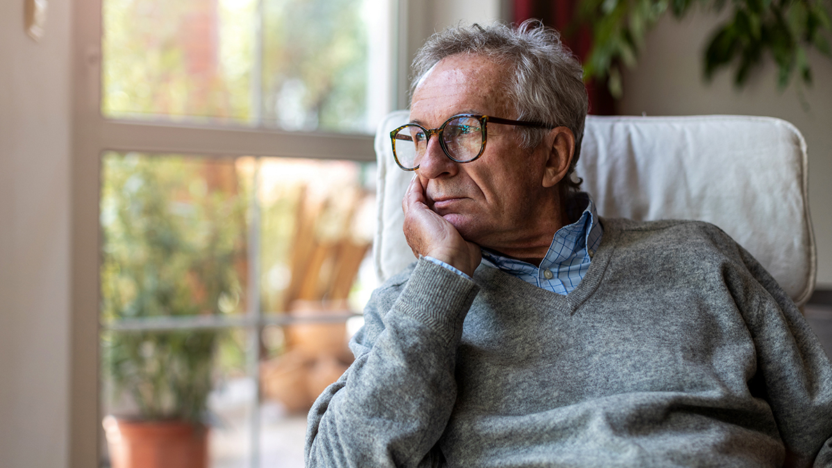 Senior Mann schaut zu Hause aus dem Fenster