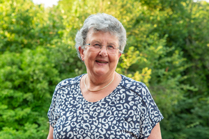 Eine ältere Dame mit grauen Haaren. Im Hintergrund Bäume
