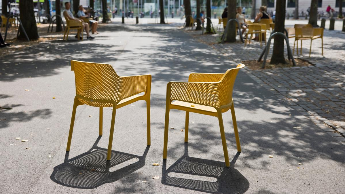 An der Ostseite des Domplatzes, dort, wo sonst entlang der Rückseite der Giebelhäuser Autos parken, stellten Münster Marketing und die Initiative Starke Innenstadt (ISI) 80 Stühle in einem warmen Sandsteingelb auf und luden die Menschen ein, diesen kleinen Teil des zentralen Platzes als "Domplatz-Oase" zu "besetzen".