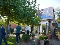 Interessierte stehen im Garten eines Wohnhauseses und lassen sich über eine auf dem Dach installierte PV-Anlage informieren