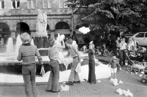 Kinder spielen ausgelassen am Lambertibrunnen. Auf dem Wasser hat sich ein großer Schaumteppich gebildet.