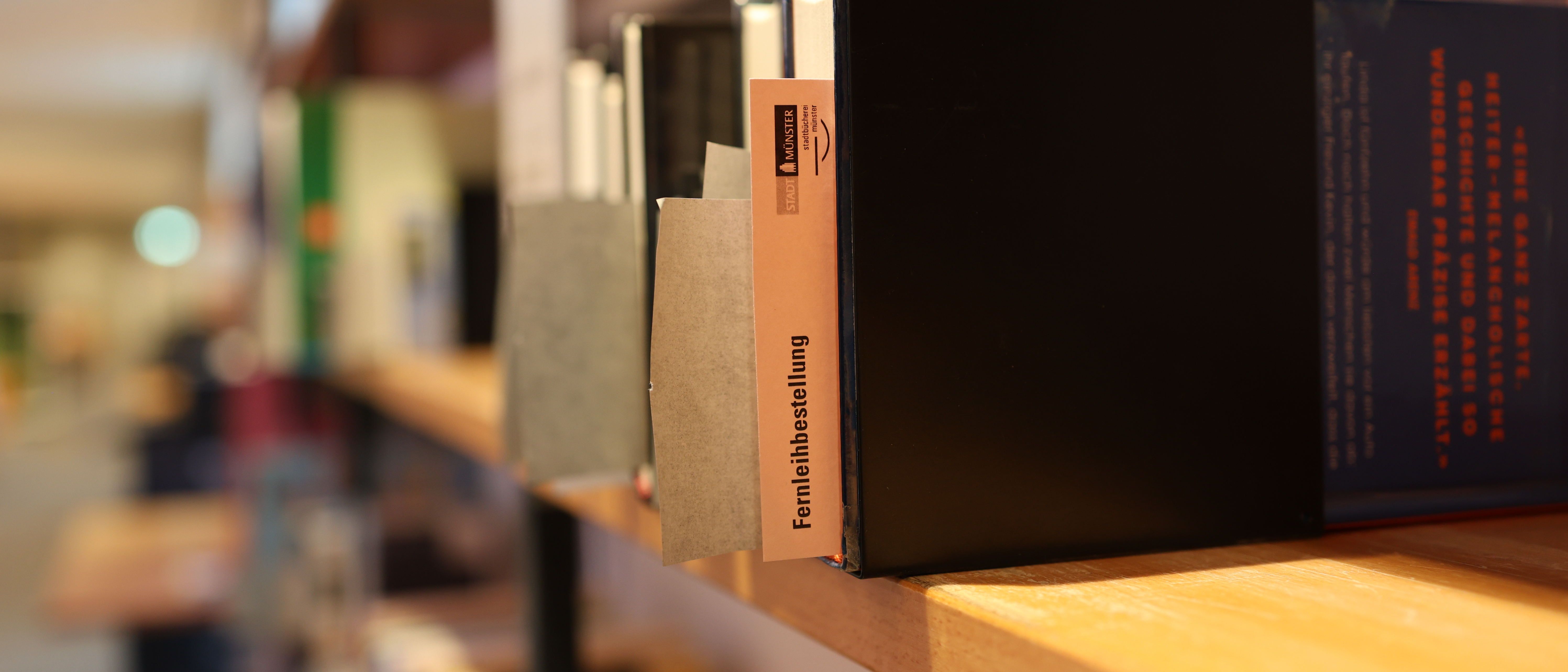 Bücherregal mit Büchern; darin ein Zettel mit der Aufschrift "Fernleihe"