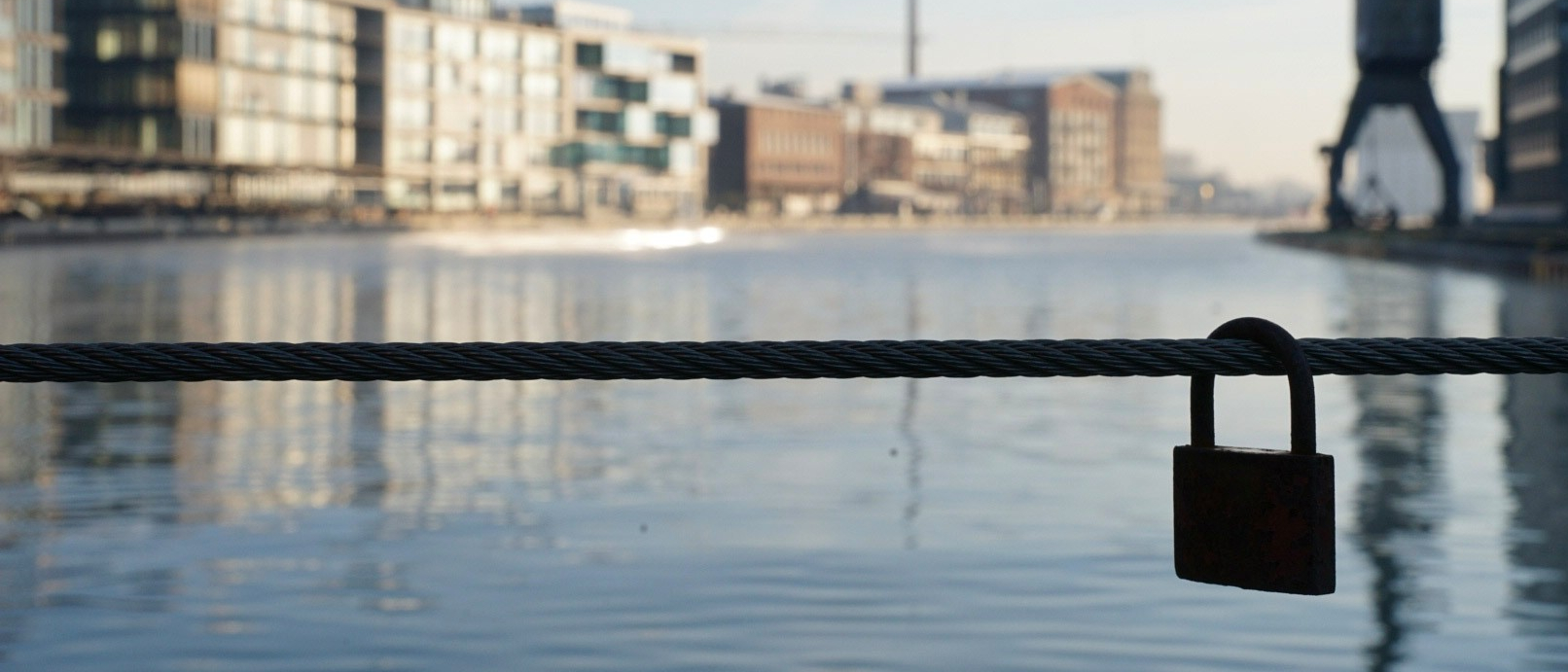 Ein Vorhängeschloss hängt an einem Geländer mit Blick auf den Hafen