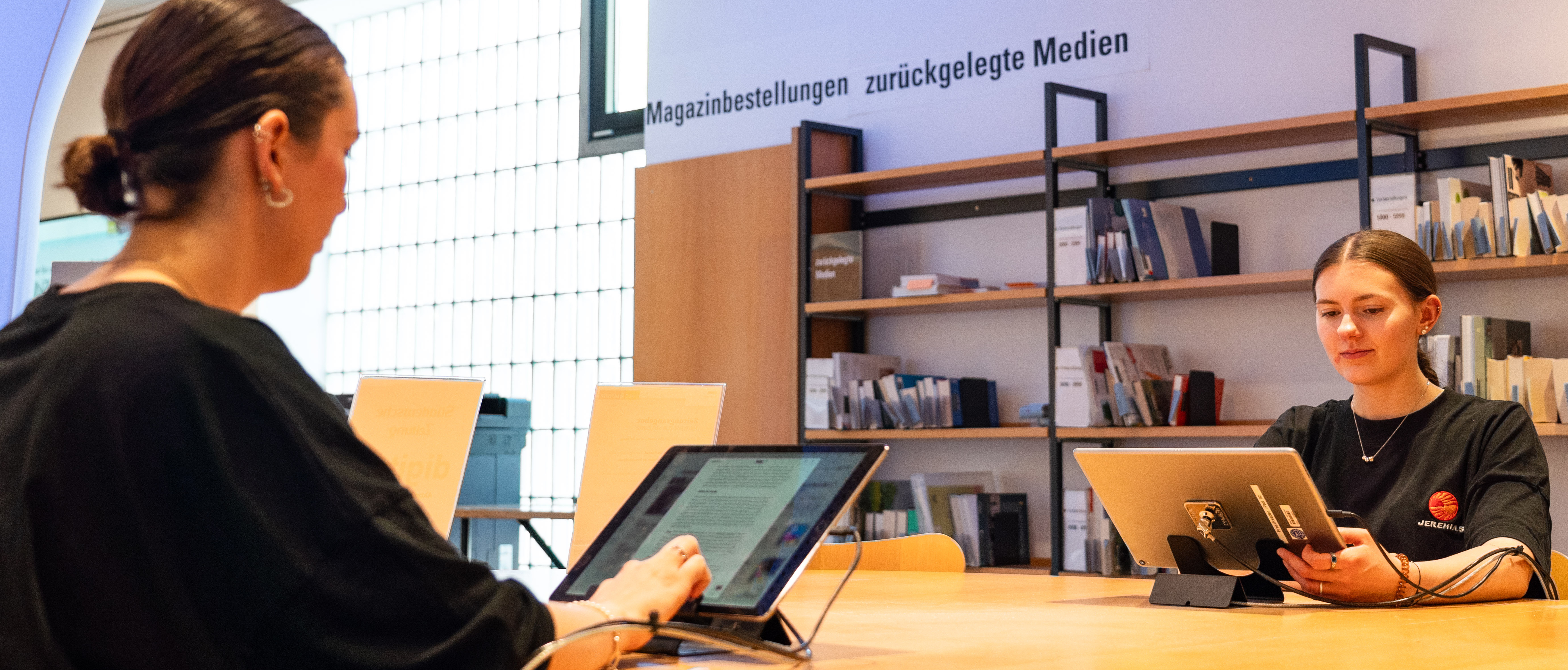 Zwei Frauen sitzen an einem Tisch und lesen auf einem Tablet