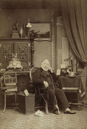 Der Fotograf Friedrich Hundt sitzt auf einem Stuhl in einem Atelier. Er schaut den Betrachter direkt an.