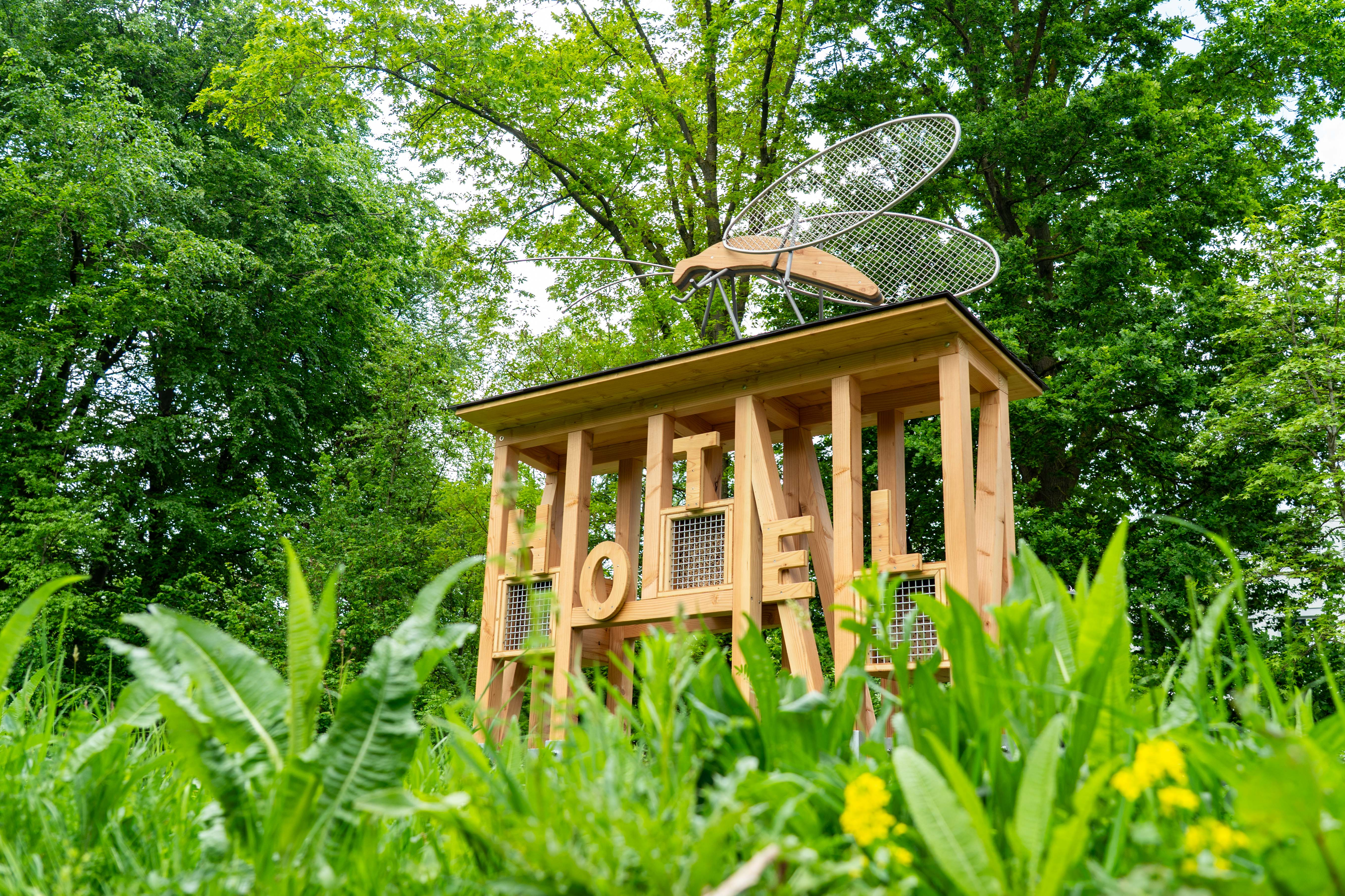 Ein Insektenhotel im neuen Naturlehrgarten an der Weseler Straße. Das Holzbauwerk hat in großen Buchstaben Hotel an der Front stehen und ein Modellinsekt sitzt auf dem Dach. 