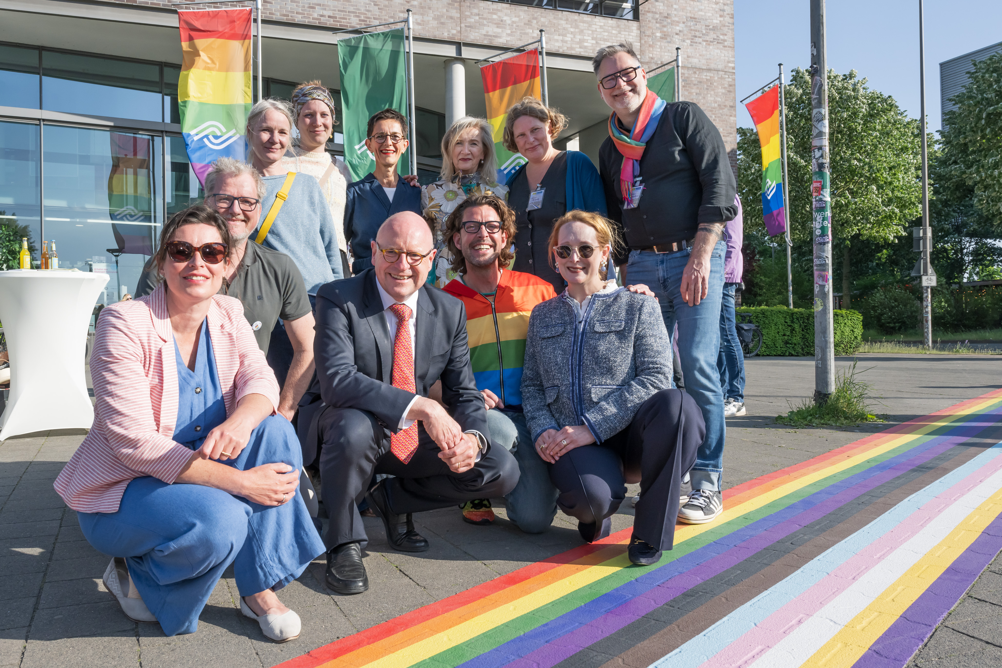 Zehn Personen hocken oder stehen neben dem Regenbogenstreifen