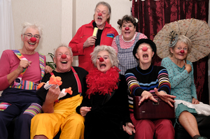 Das Ensemble ‚Clown Compagnie plusminus‘ sitzt lachend auf einem Sofa. Alle im Ensemble tragen eine rote Nase.