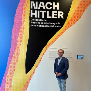Ein Mann im Anzug steht vor einer Wand. Auf der Wand steht "Nach Hitler".