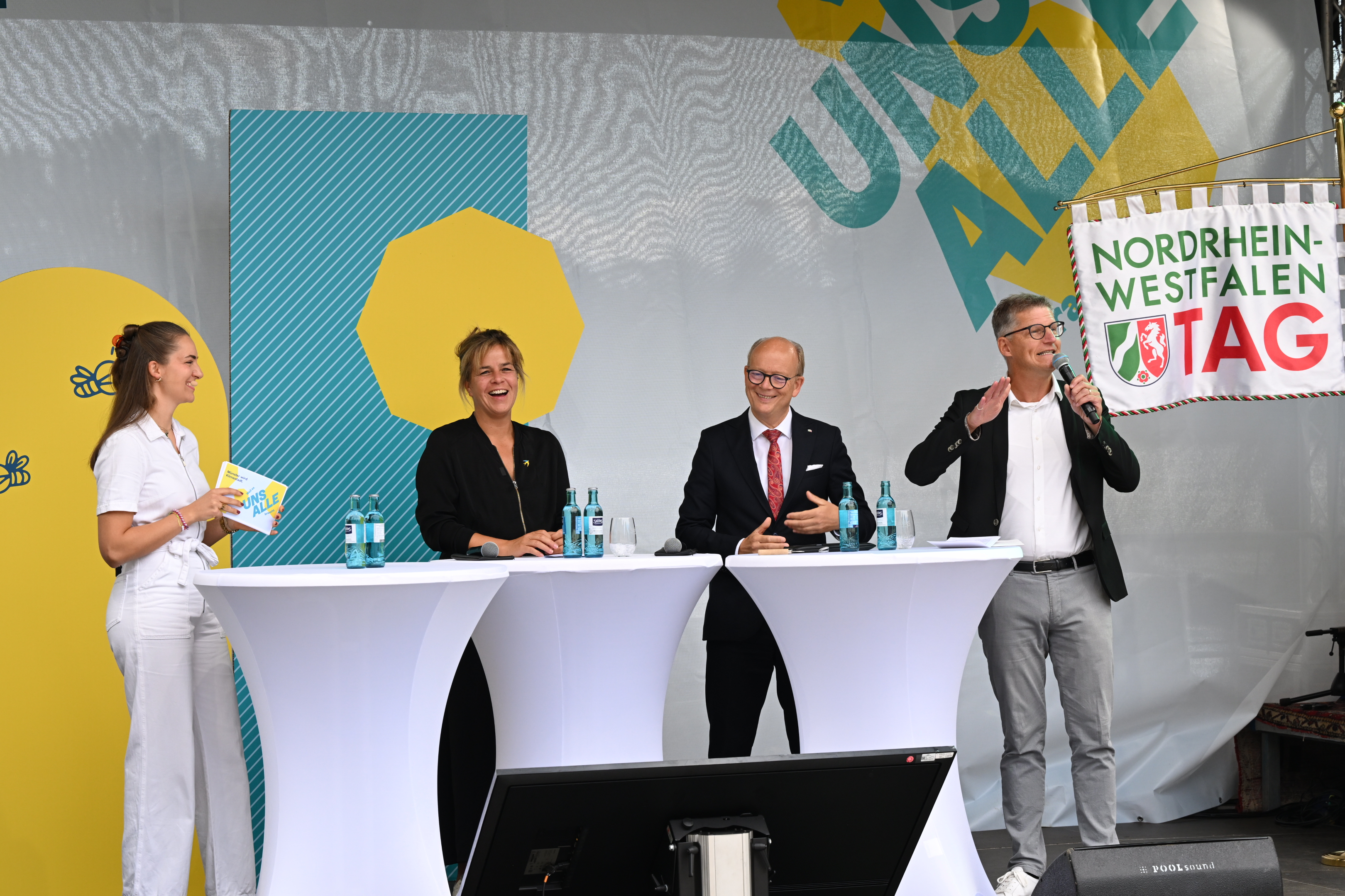 Mona Neubaur, stellvertretende Ministerpräsidentin des Landes Nordrhein-Westfalen und Landesministerin für Wirtschaft, Industrie, Klimaschutz und Energie, André Kuper, Präsident des Landtags Nordrhein-Westfalen, und Oberbürgermeister Tilman Fuchs stehen auf einer Bühne