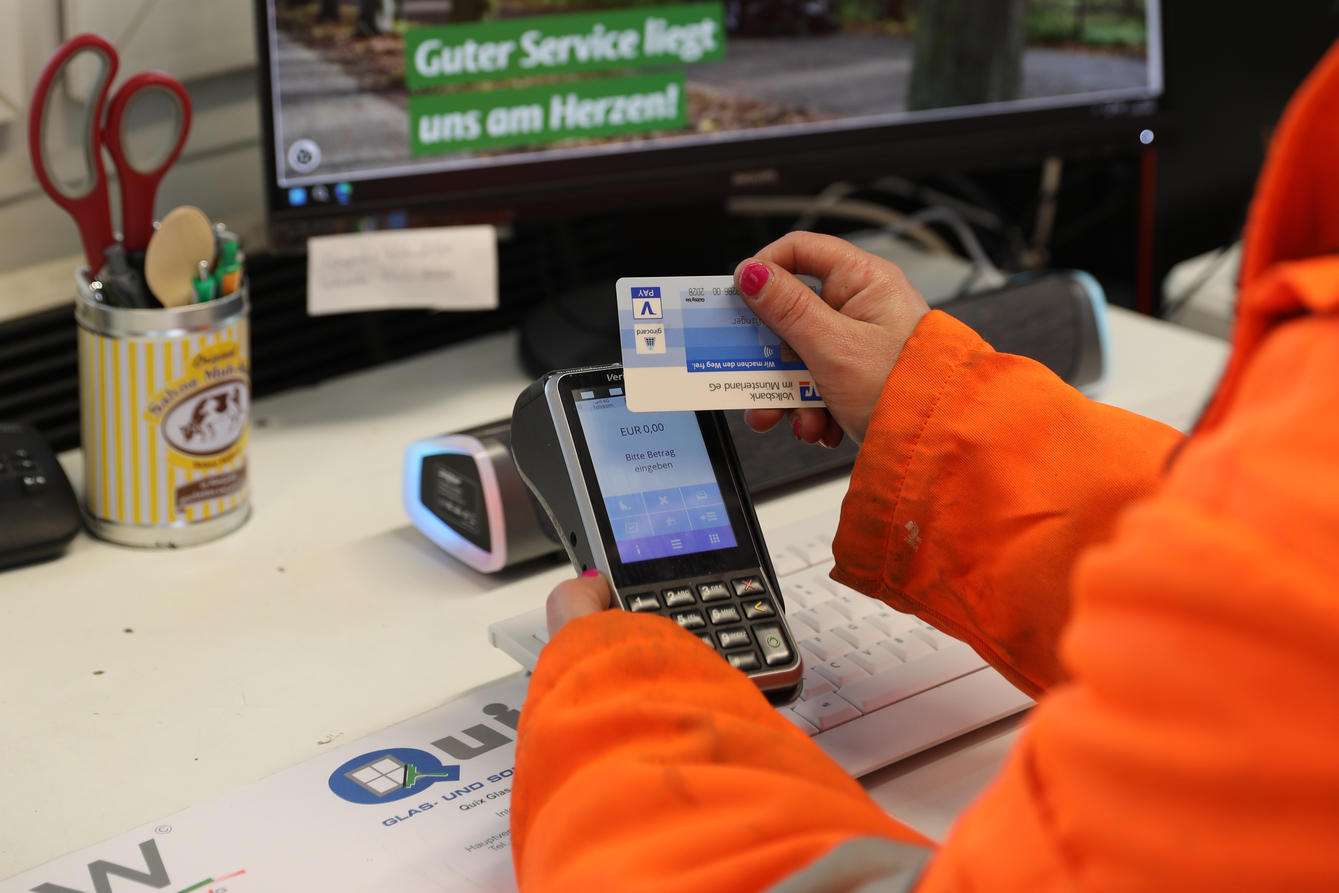 An einem Schreibtisch im Büro oder Kassenhäuschen eines Recyclinghofs wird mit Karte gezahlt.