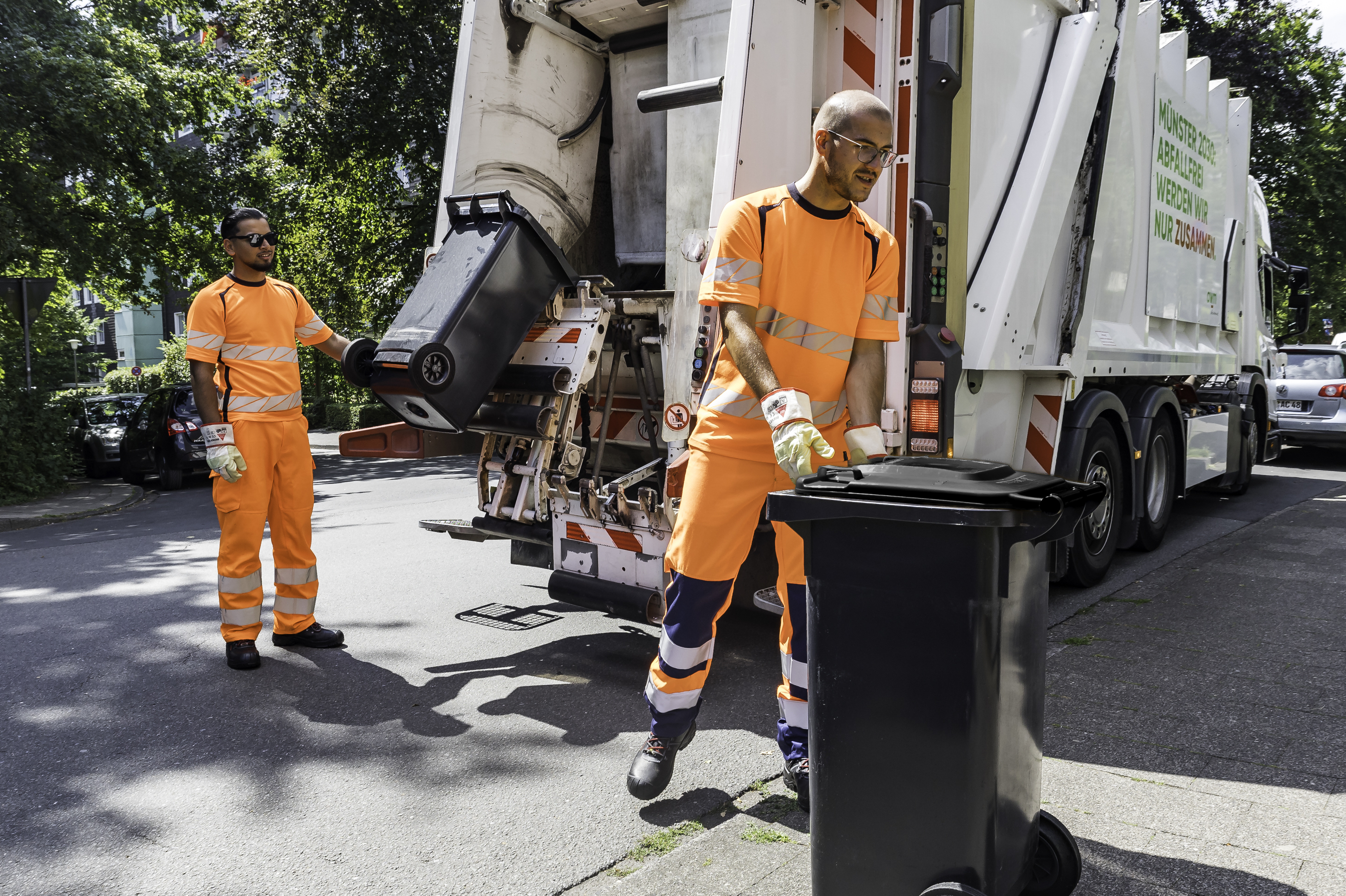 Zwei Männer leeren Abfalltonnen mithilfe eine Abfuhrfahrzeuges