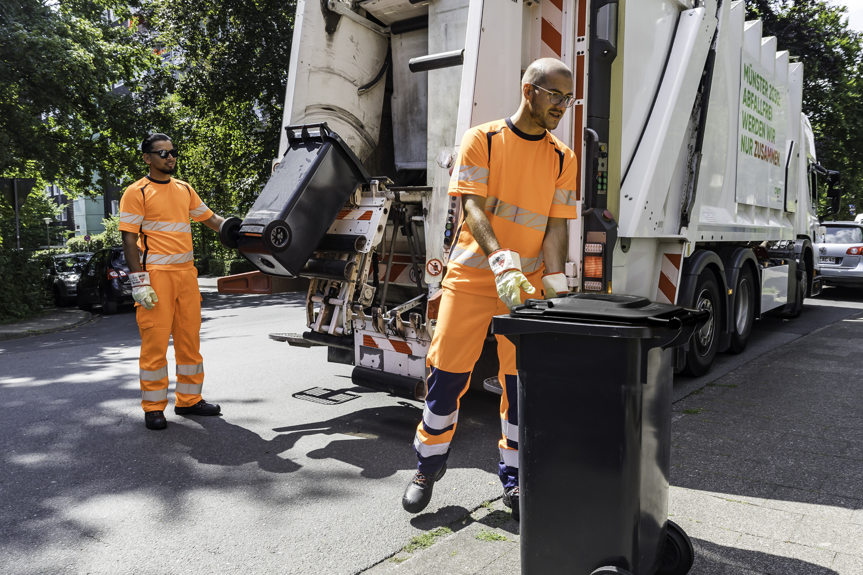 Zwei Männer leeren Abfalltonnen mithilfe eine Abfuhrfahrzeuges