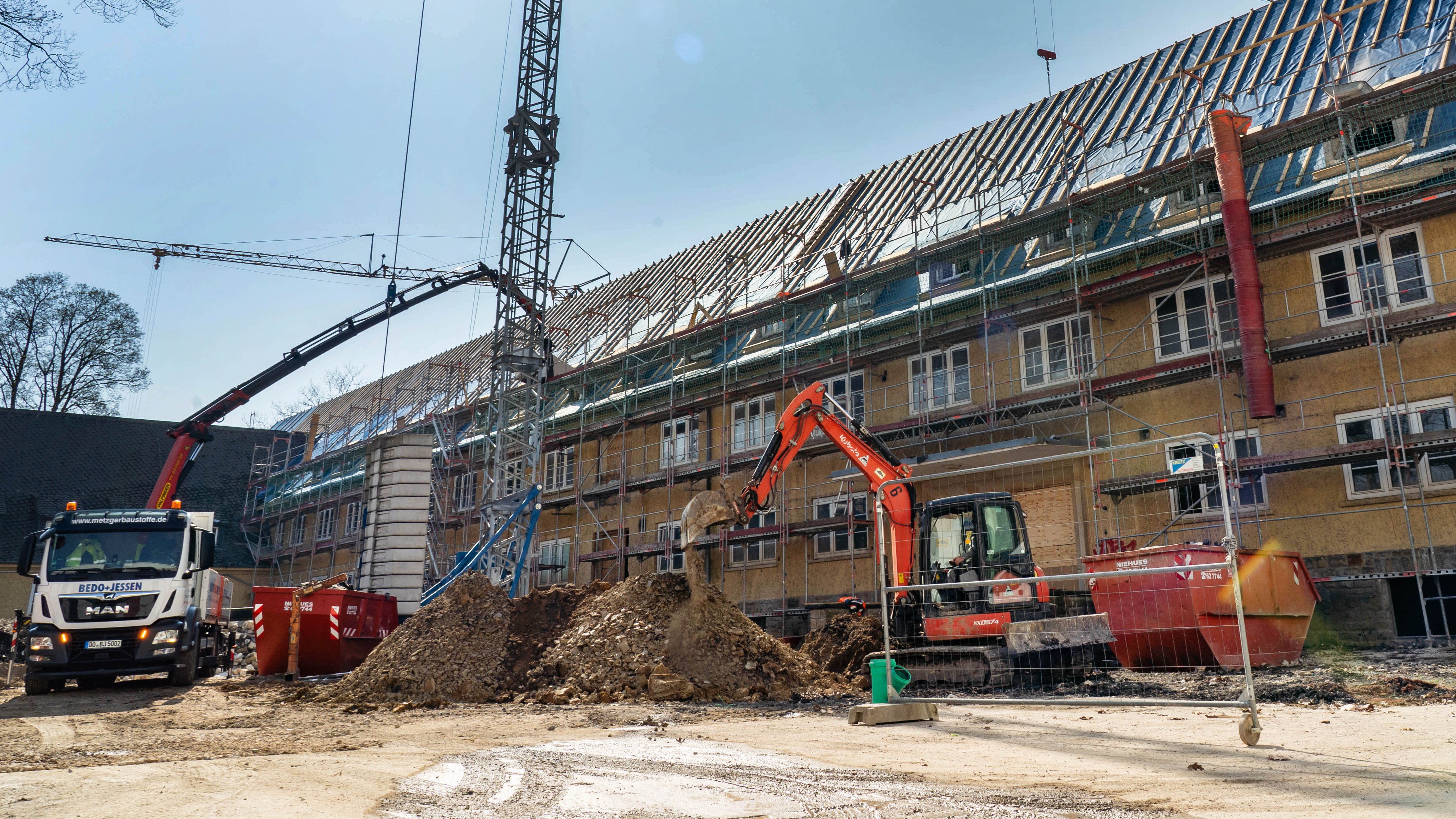 Blick auf die Baustelle des Gebäudes mit Baukran, Bagger, LKW und Baugerüst
