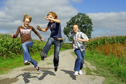 3 Junge Menschen hüpfen über einen Feldweg zwischen Feldern
