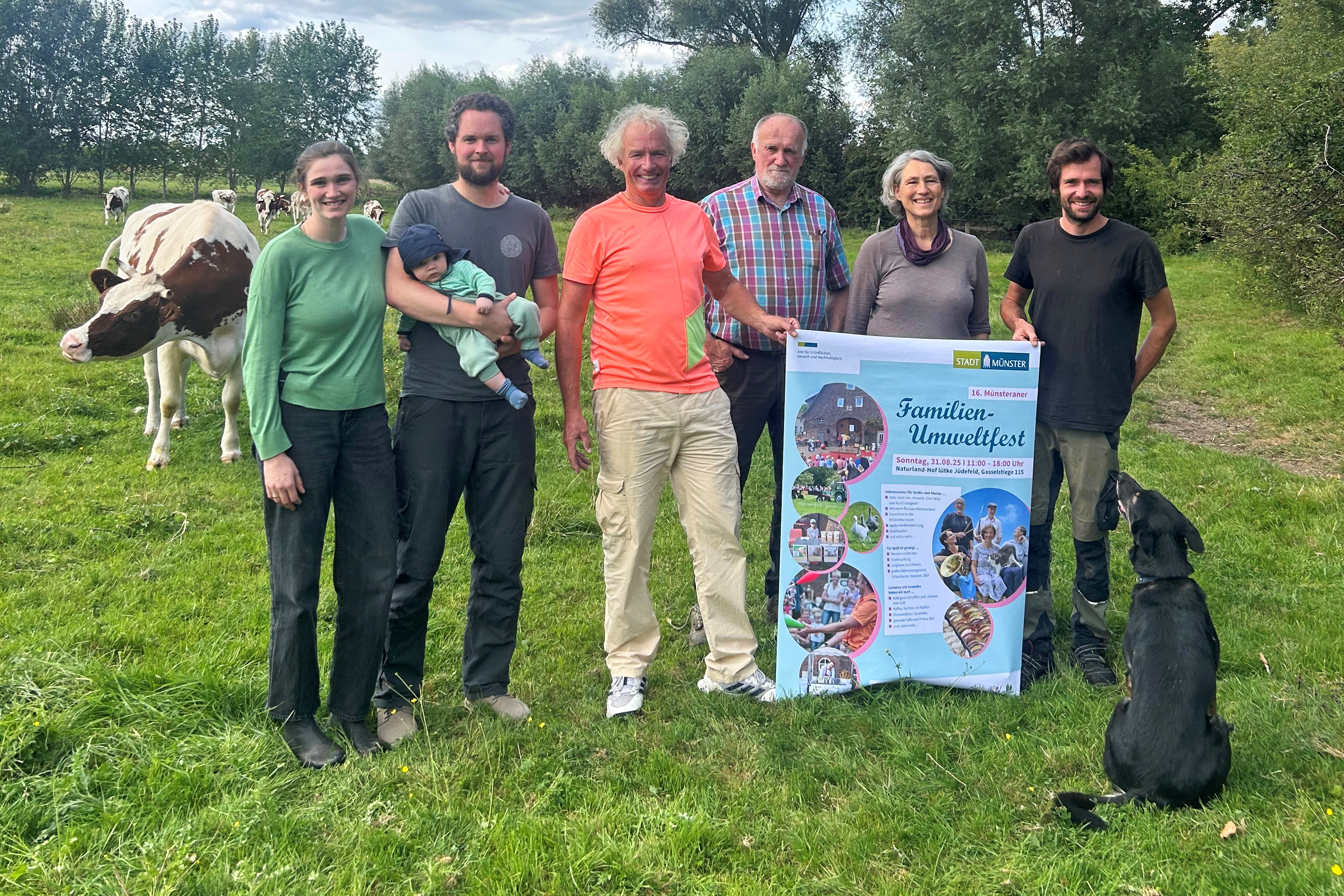 Sieben Personen und ein Hund auf einer Rinderweide mit Veranstaltungsplakat