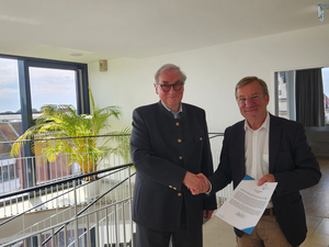 Wolfgang Heuer und Horst Wiechers stehen nebeneinander und geben sich die Hand, Heuer hält eine Urkunde in der Hand.