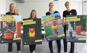 Vier Studierende der FH Münster halten Plakate mit dem Siegerentwurf "Zeig dich von deiner Schokoladenseite" in der Hand