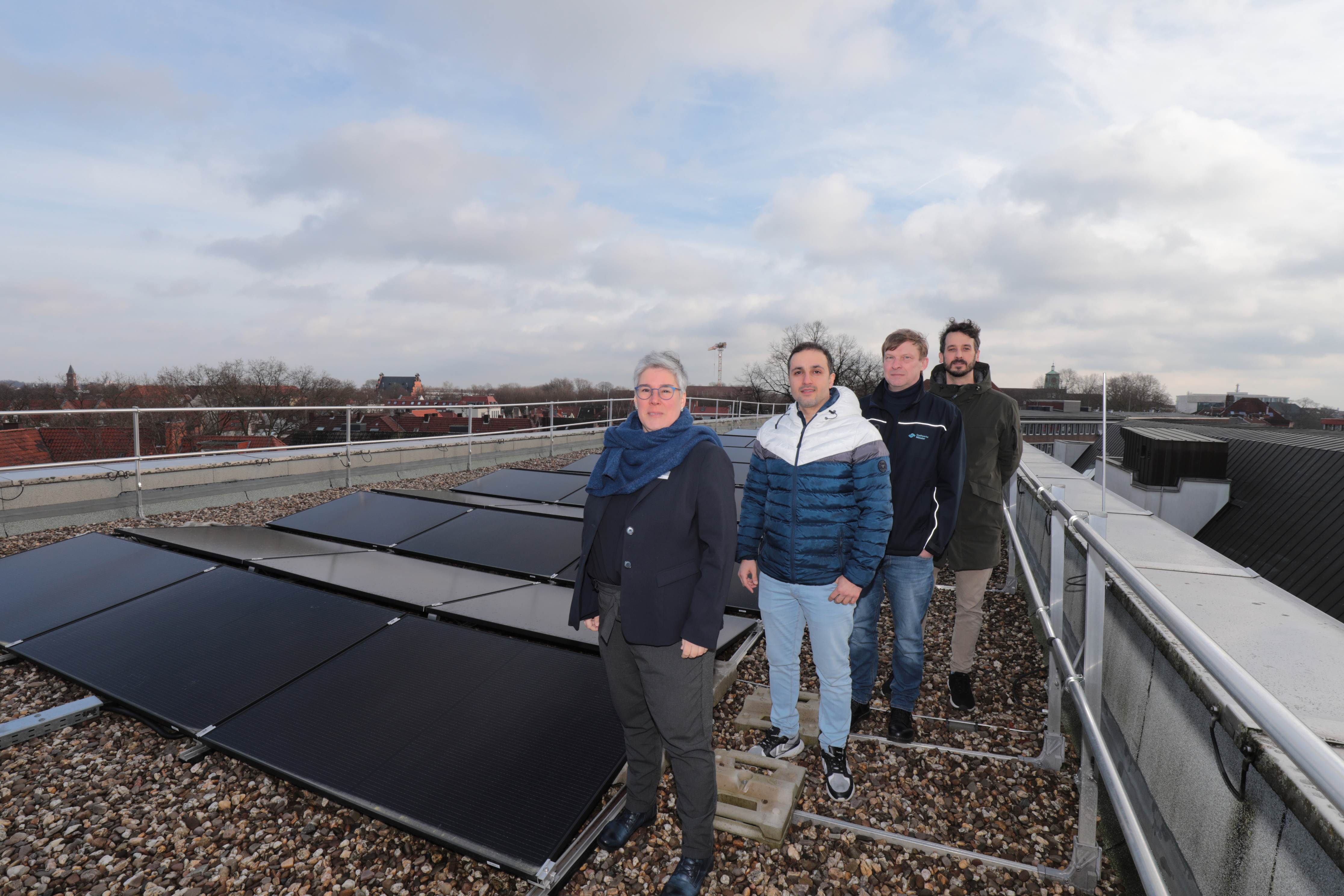 Vier Personen stehen neben der Photovoltaik-Anlage auf dem Dach der Stadtbücherei